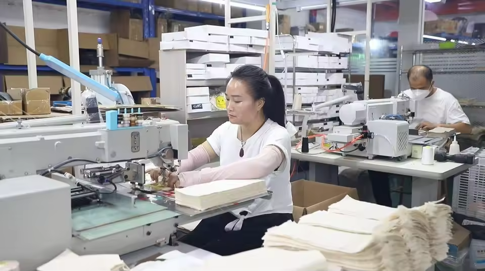 Factory workstation with worker assembling and inspecting small jewelry packaging components — illustrating the precision production required for brooch insert fabrication