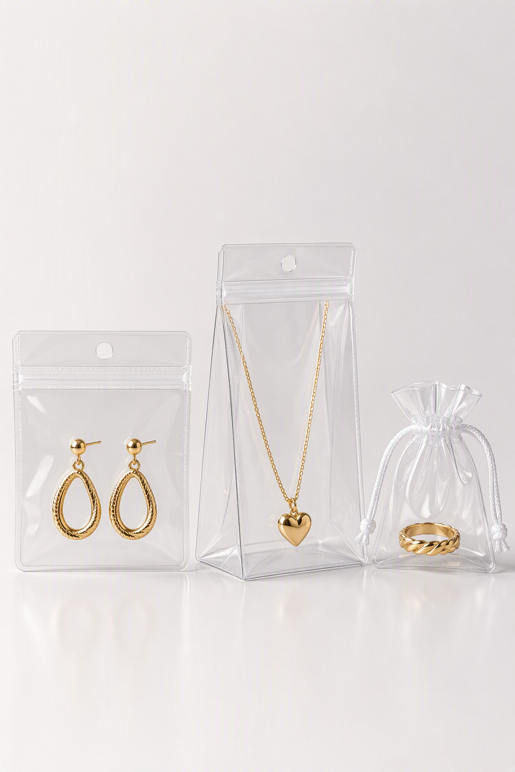 Clear transparent PVC jewelry bags holding earrings, a necklace, and a ring on a white studio surface