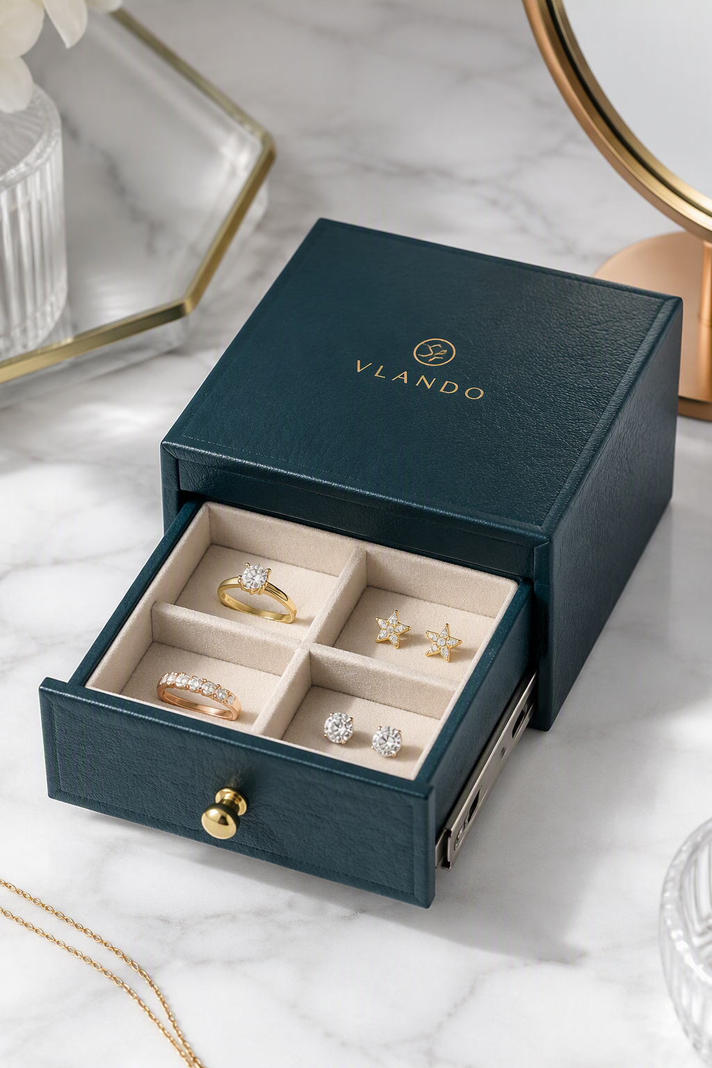 PU leather drawer jewelry box in deep teal with gold foil logo, drawer open revealing 2x2 flocked grid with rings and stud earrings